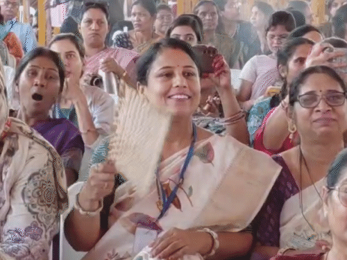 गर्मी से बचने के लिए एक कार्यकर्ता हाथ का पंखा लेकर आई है।