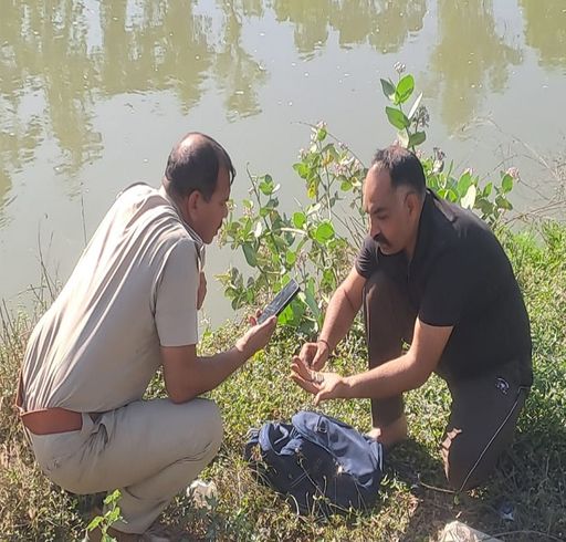 नहर किनारे पड़े लड़के के बैग को चेक करते पुलिस अधिकारी। (फोटो 15 अप्रैल की है)