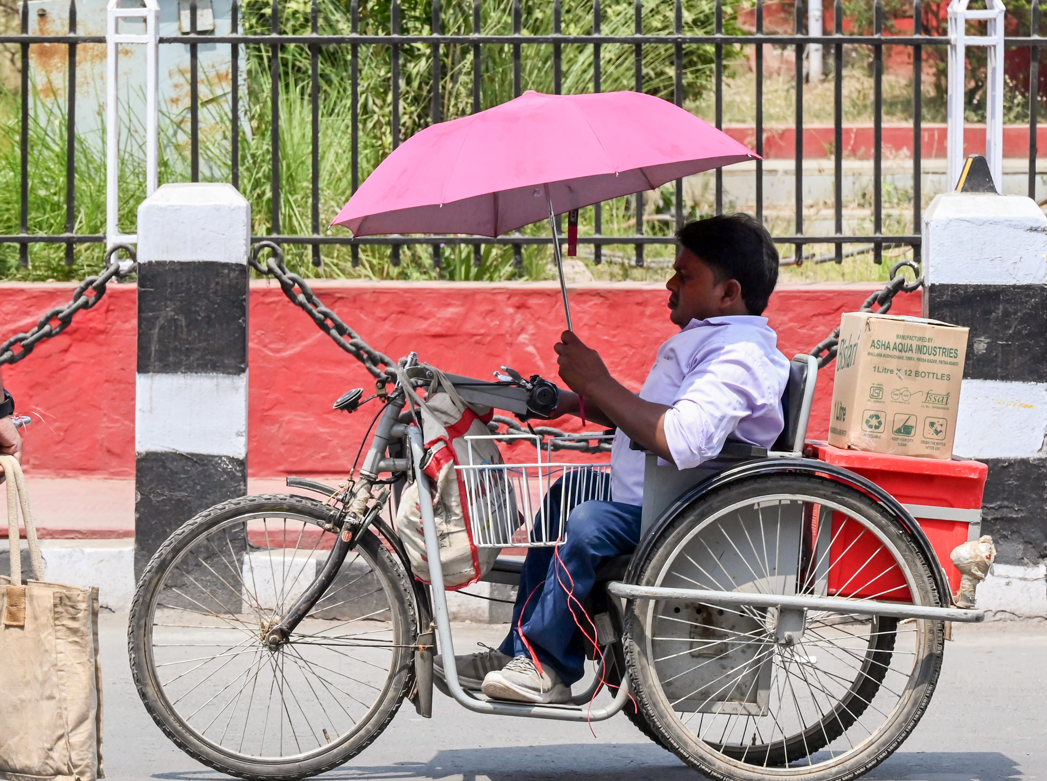 पटना में ट्राइसिकिल पर छाता लगाकर धूप से बचाव करता एक दिव्यांग।