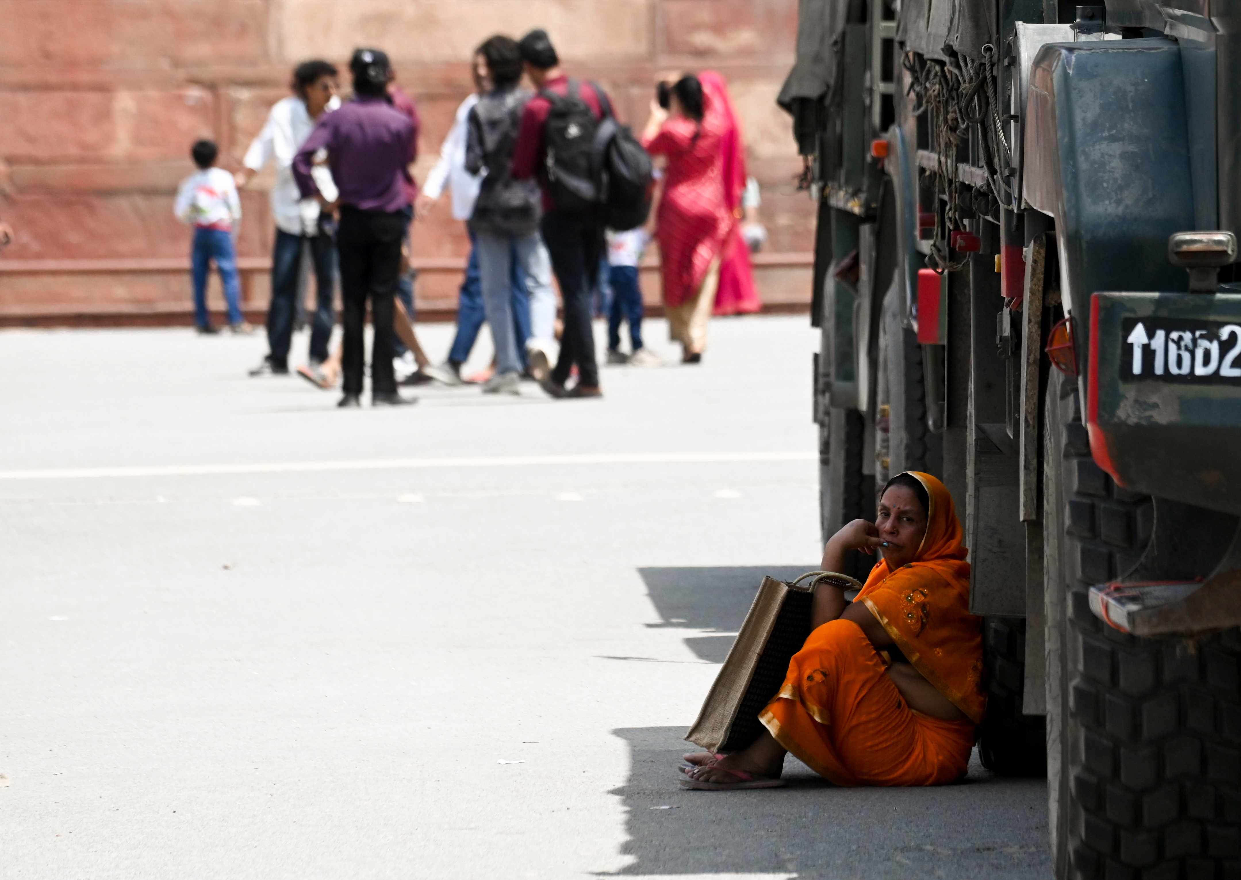 दिल्ली में 43.5°C तापमान में आर्मी व्हीकल की छांव में बैठकर तपिश से राहत पाती एक महिला।