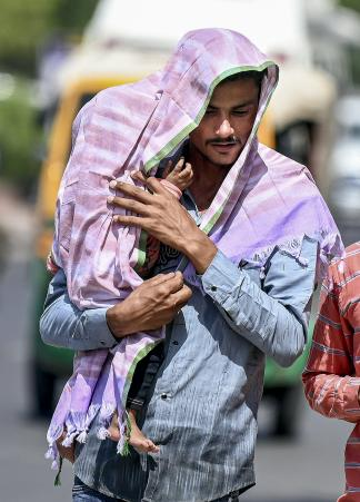 राजस्थान के बीकानेर में पारा 44.2°C होने के बाद बच्चे को धूप से बचाता एक शख्स।