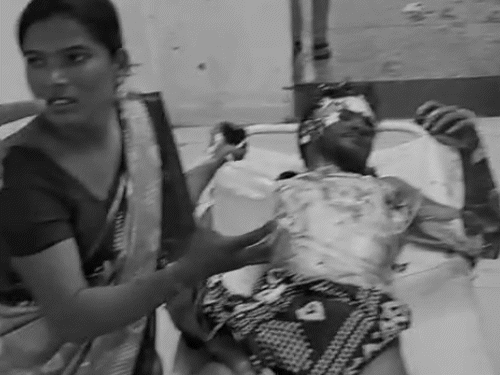 अस्पताल के बेड पर दर्द से तड़पता घायल। पास बैठी महिला मदद मांगती रही।