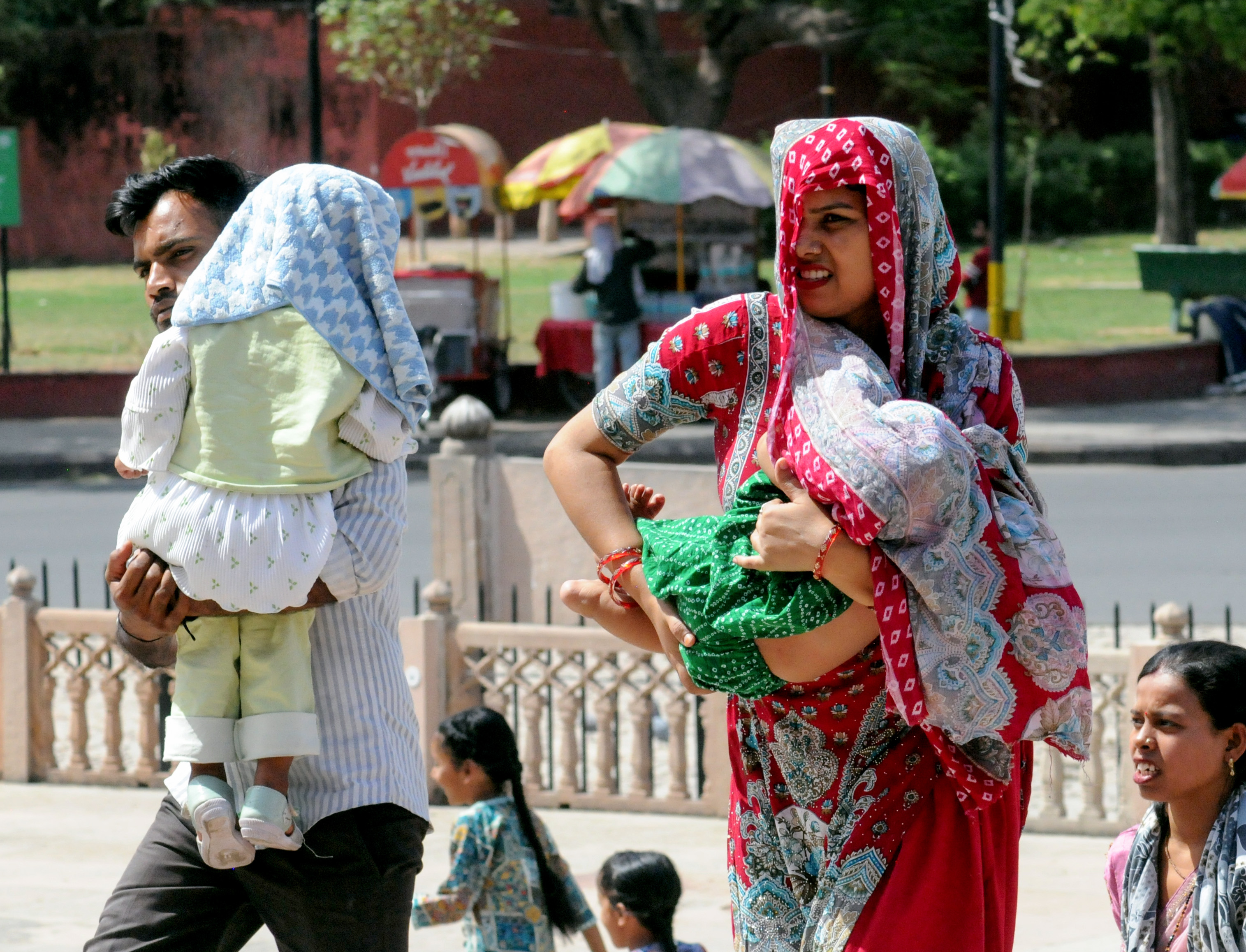 जयपुर में बच्चों को तेज धूप से बचाने के लिए ढंककर ले जाते माता-पिता।
