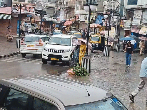 मंडी में बारिश के बीच चलते हुए लोग और वाहन।