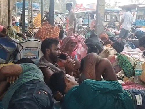 गर्मी में सड़क किनारे बैठे लोग। पास में पड़ा उनका सामान।