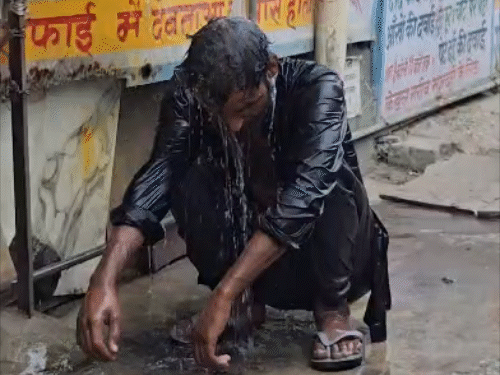 गर्मी में पानी की टंकी के नीचे बैठकर नहाता युवक।