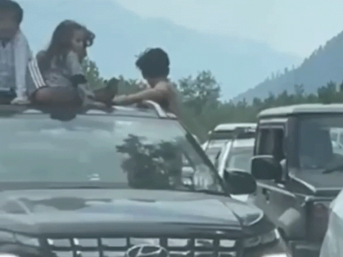 गाड़ी के सनरूफ पर बैठे बच्चे।