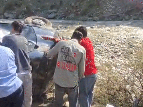 कुल्लू के मणिकर्ण में गाड़ी में फंसे लोगों को बाहर निकालते हुए स्थानीय लोग।
