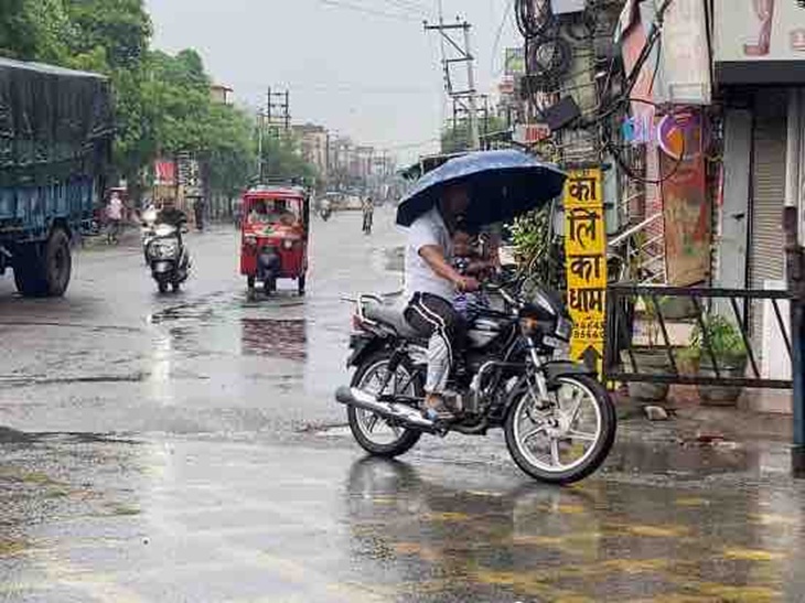 जालंधर में बारिश के बीच छाता ओढ़कर बाइक पर जाता युवक।