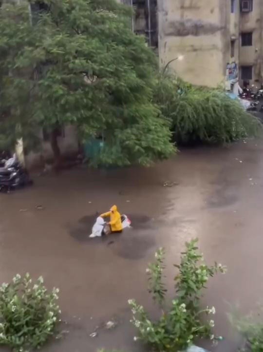 बारिश की वजह से कॉलोनी में बाइक के साथ फंसा व्यक्ति।