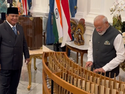 इंडोनेशिया के पारंपरिक संगीत वाद्ययंत्र अंगक्लुंग बजाने की कोशिश करते हुए पीएम मोदी। साथ में ताली बजाते हुए राष्ट्रपति प्रबोवो सुबियांतो। - Dainik Bhaskar
