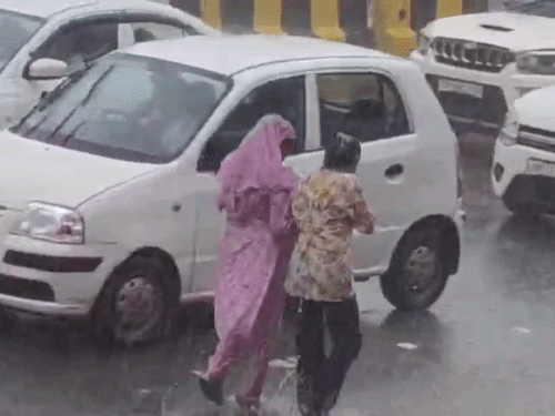 गुरुग्राम में बारिश के दौरान भीगते हुए निकलती युवतियां।