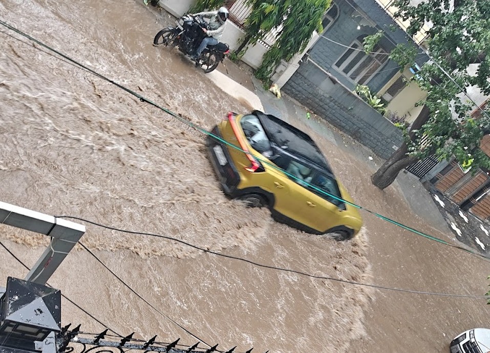 गुरुग्राम के सुशांत लोक इलाके में घरों के बाहर भरे बारिश के पानी से निकलती गाड़ियां।