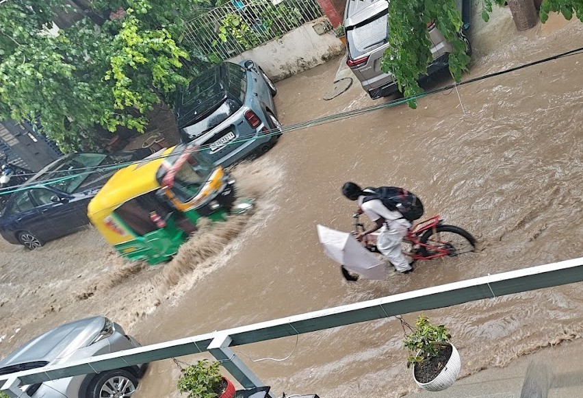 गुरुग्राम के सुशांत लोक इलाके में घरों के बाहर भरे बारिश के पानी से निकलती गाड़ियां।