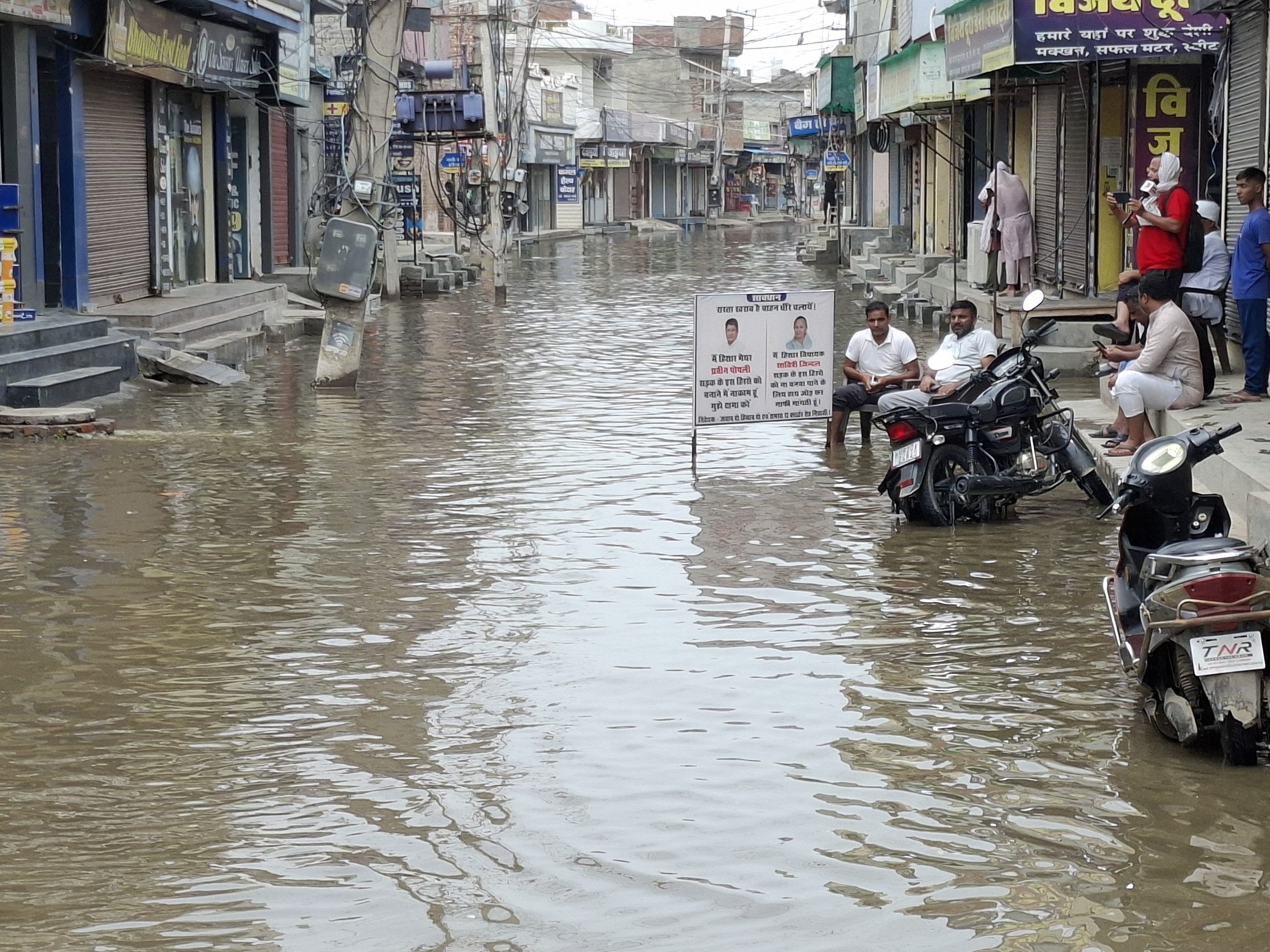 हिसार में सड़क पर भरे पानी के बीच, विधायक और मेयर का बैनर लगाकर रोष जाहिर किया।