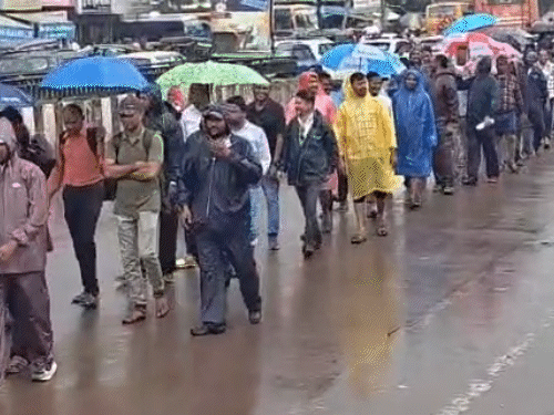 शिक्षकों ने बारिश के बीच छाता लेकर रैली निकाली।