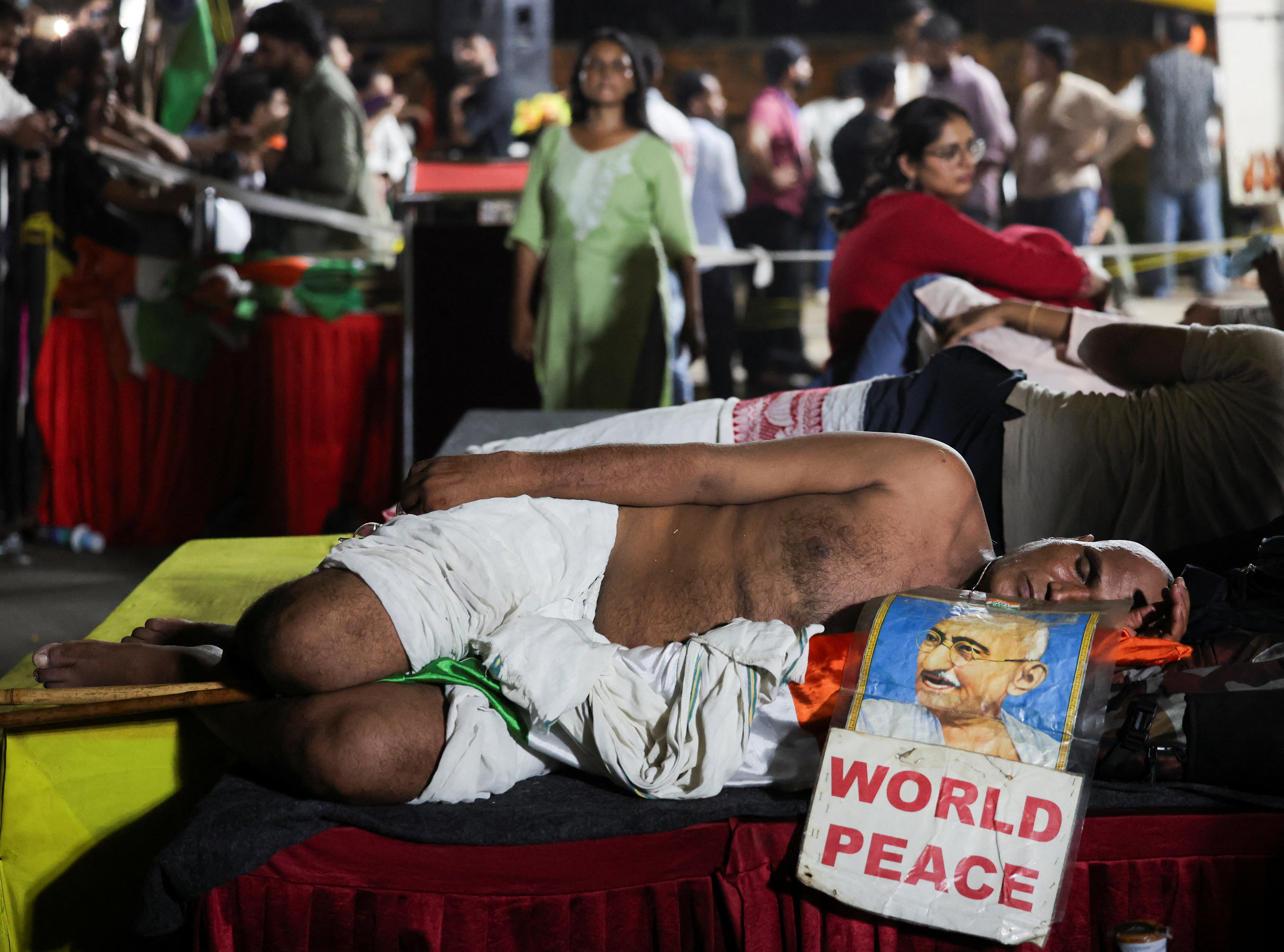 Near the stage built at Jantar Mantar, an elderly person is sleeping with a photo of Mahatma Gandhi. The photo has 'World Peace' written on it.
