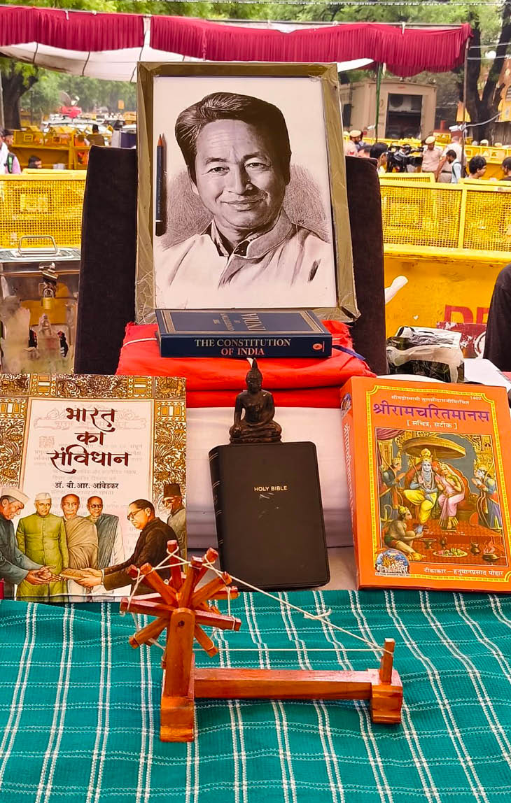 जंतर-मंतर पर चल रहे प्रदर्शन के दौरान मंच पर सोनम वांगचुक की फोटो, संविधान की कॉपी, चरखा, बाइबिल, बुद्ध की प्रतीमा और रामचरितमानस रखी गई है।