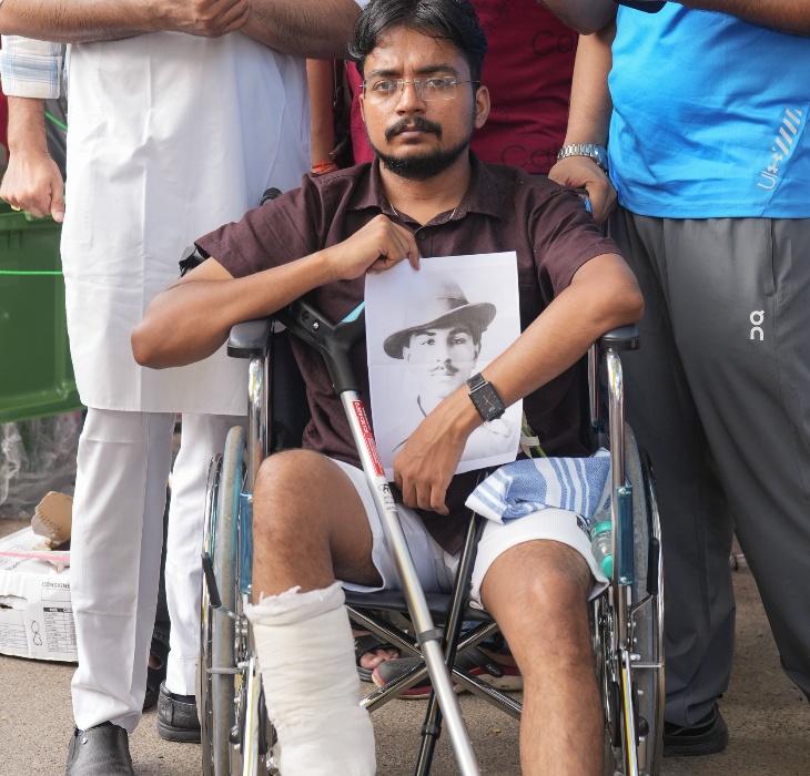 दिल्ली में संसद मार्च लाठीचार्ज में घायल प्रदर्शनकारी भगत सिंह की तस्वीर लिए हुए और पैर पर प्लास्टर बांधे हुए दोबारा प्रदर्शन में शामिल हुआ।