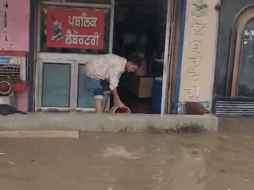 दुकान में घुसे पानी को बाहर निकालता दुकानदार।