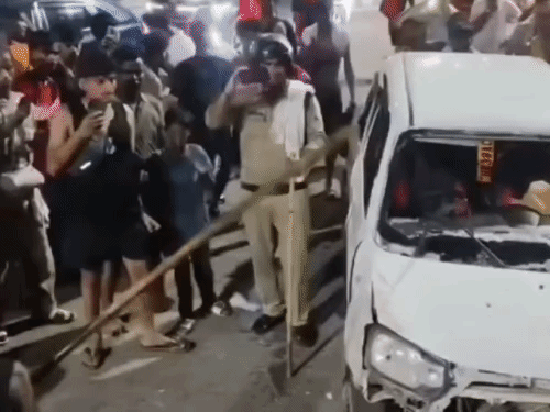 The accused breaking the car with a stick in front of the police. He hit the car's bonnet and windows multiple times.