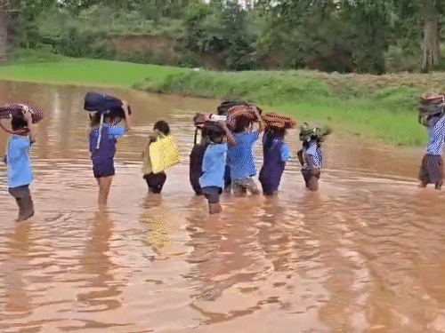 Children in Gariaband, Chhattisgarh, crossing waterlogged paths with bags on their heads to go to school.