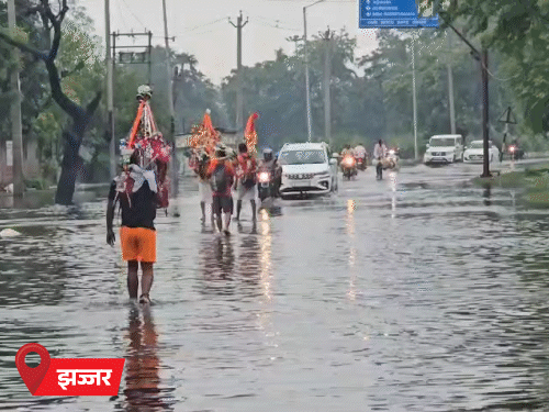 झज्जर में बरसाती पानी के बीच कांवड़ियों की आस्था जारी। सड़क पर हुए जलभराव से निकलते हुए कांवड़िए।