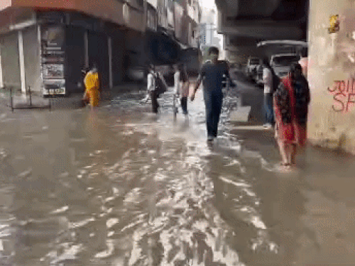 शीला बाईपास पर सड़क पर भरे पानी से गुजरते लोग।