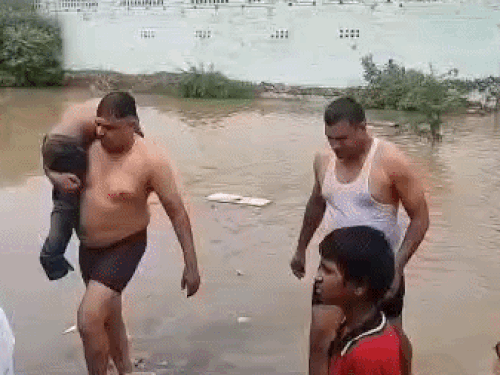 राजीव कॉलोनी में बच्चे के शव को पानी से निकालकर लाते हुए लोग।