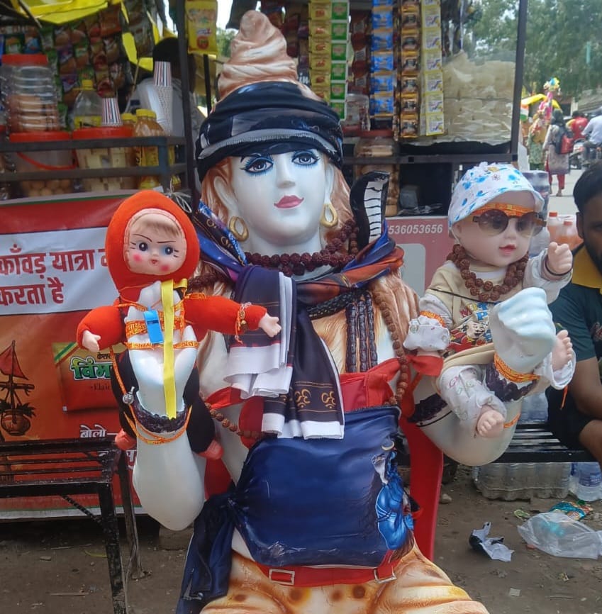ईशु उर्फ फौजी रतनगढ़िया कंधों पर भगवान भोलेनाथ की प्रतिमा रखकर पैदल चल रहे हैं और प्रतिमा के दोनों कंधों पर एक लड़के और एक लड़की की डॉलनुमा तस्वीरें लगाई गई हैं।