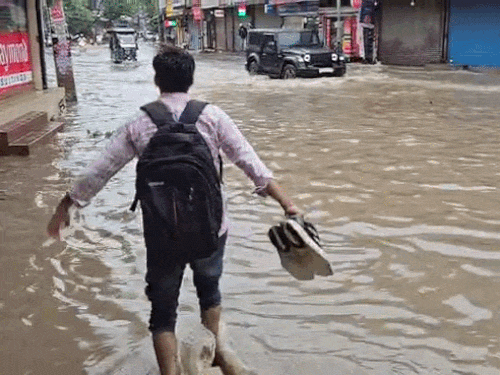 सोनीपत में जलभराव के दौरान जूते हाथ में लेकर सड़क पार करता युवक। - Dainik Bhaskar