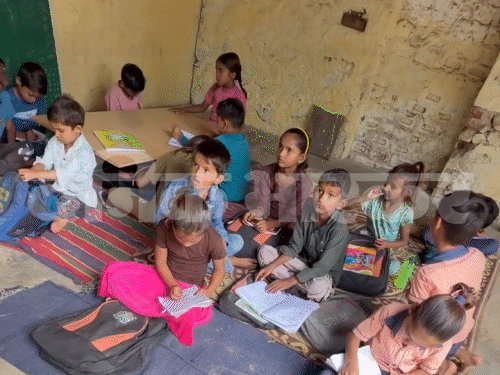 बाड़े में जमीन पर बैठकर पढ़ते हैं बच्चे।