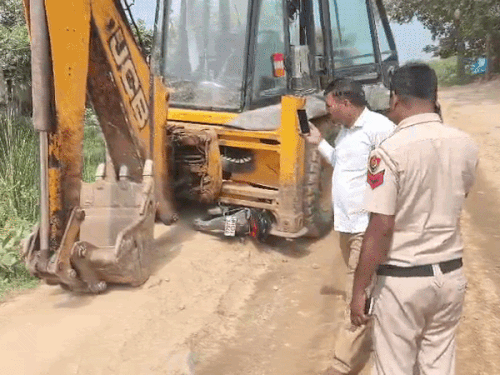 जेसीबी के नीचे पड़ी बाइक की जांच करते पुलिस कर्मी