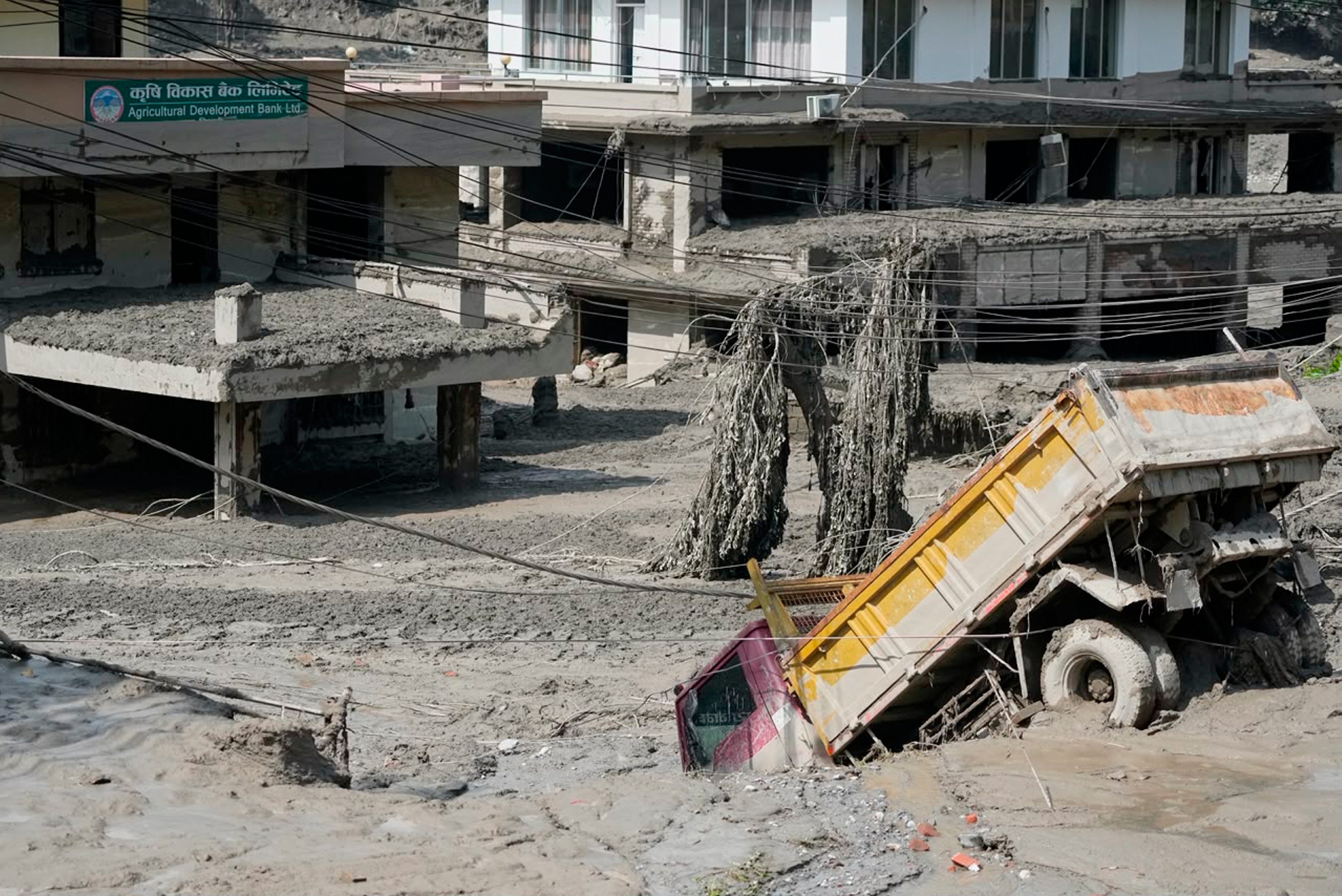 नुवाकोट जिले में त्रिशूली नदी के किनारे अचानक आई बाढ़ के बाद क्षतिग्रस्त घर और वाहन नजर आए।