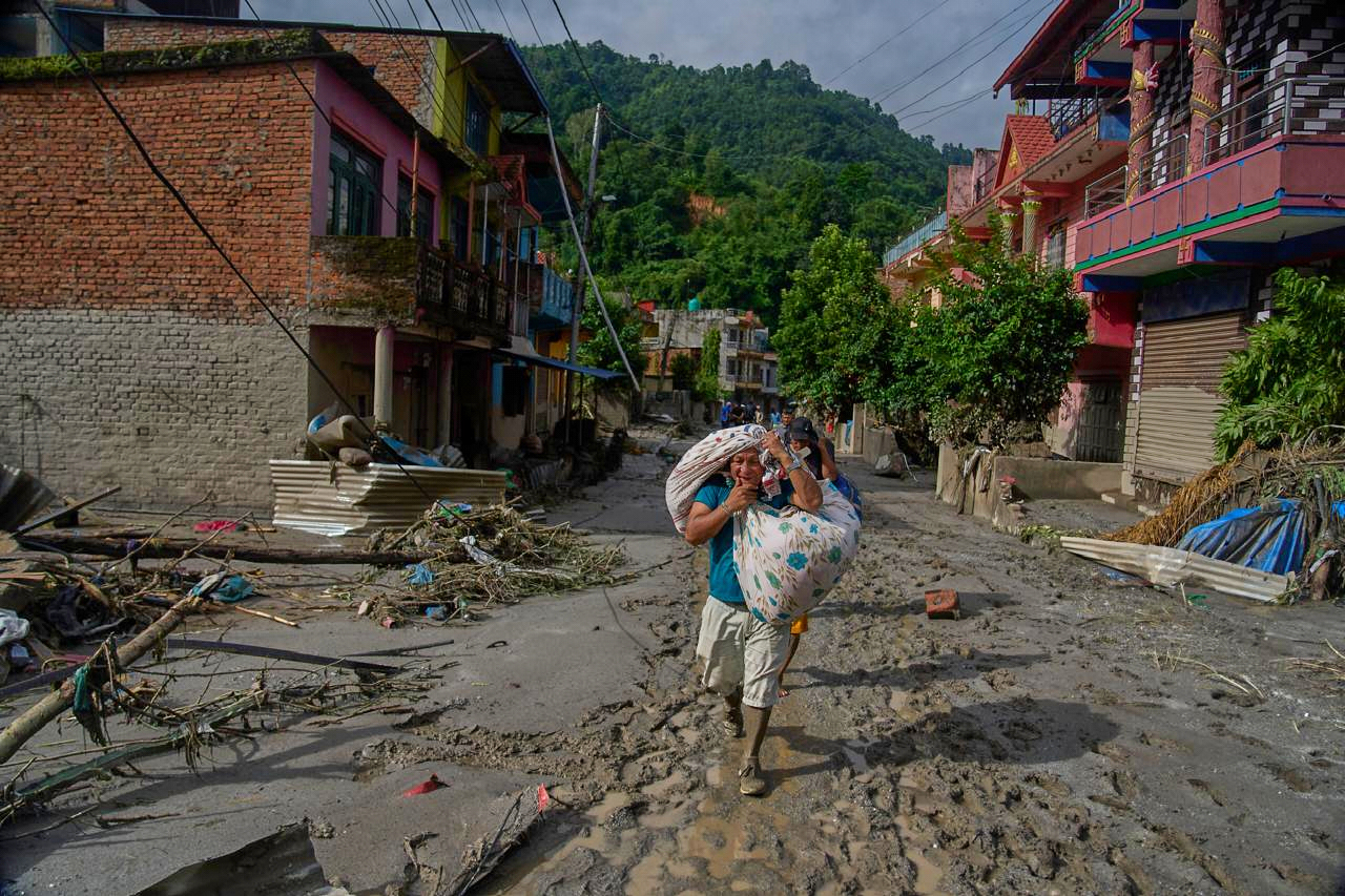 नुवाकोट जिले के देवीघाट में सुरक्षित जगह की ओर जाते स्थानीय लोग अपना सामान लेकर निकलते हुए।
