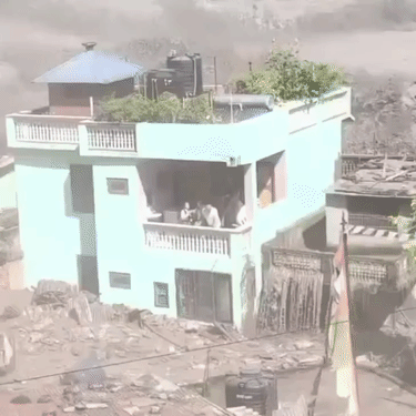 बाढ़ के पानी और मलबे में एक घर पूरी तरफ से घिर गया। उसके दोनों तरफ से पानी बह रहा है।