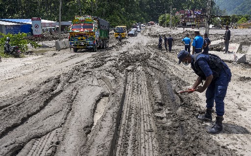 एक सुरक्षाकर्मी धादिंग में बाढ़ के बाद सड़क पर जमा कीचड़ और मलबा हटाता हुआ।