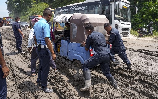 सड़क पर जमा कीचड़ और मलबे में फंसे एक ऑटो-रिक्शा को निकालने की कोशिश करते पुलिसकर्मी।
