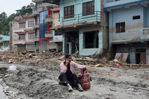 एक महिला बाढ़ प्रभावित इलाके में गैस सिलेंडर के पास बैठकर फोन पर बात करती हुई।