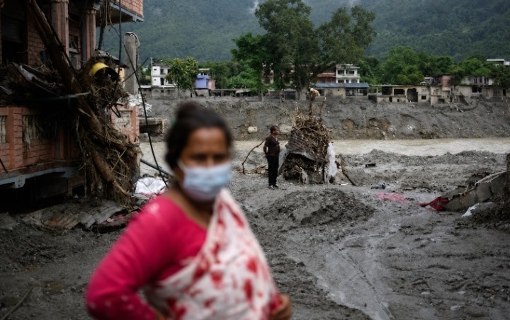 एक महिला बाढ़ के बाद मलबे और कीचड़ से घिरे इलाके में खड़ी हुई।