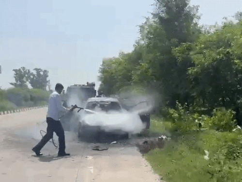 कार में लगी आग को बुझाते कर्मी।