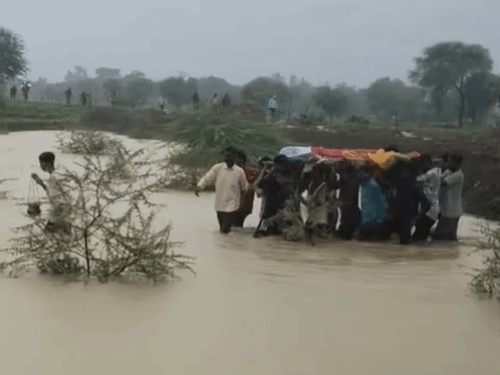 Villagers wade through waist-deep water to reach the cremation ground in Semariya village, Durg district, Chhattisgarh.