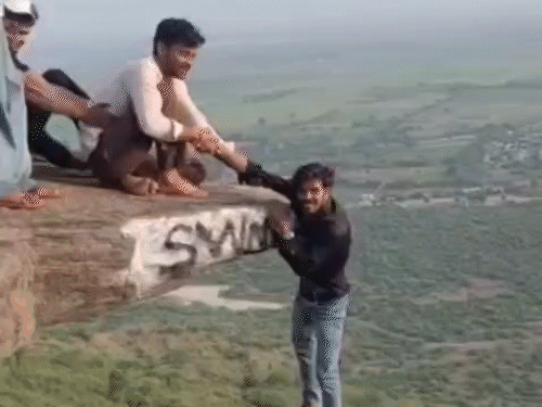 रील बनाने के लिए युवक ने एक हाथ दोस्तों को थमाया और पहाड़ी से लटककर दूसरे हाथ से विक्ट्री का साइन बनाया।