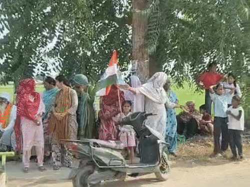स्कूली बच्चे और महिलाएं गांव के एंट्री साइड में तिरंगा लेकर खड़े हुए हैं।