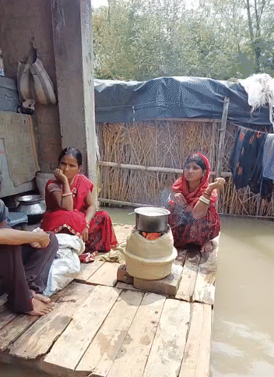 खगड़िया में बाढ़ के पानी के बीच चौकी पर चूल्हा रखकर खाना बनाती महिलाएं।