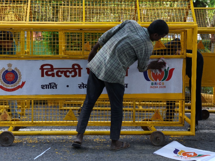 बैरिकेड्स पर ब्रिक्स के लोगो का पोस्टर लगाता एक व्यक्ति।