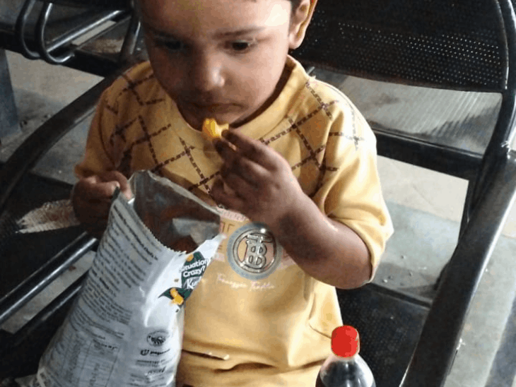 बस स्टैंड पर बच्चा अकेला बैठा चिप्स खाता हुआ।