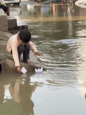 नन्हा बच्चा बाहर खेल नहीं सकता, इसलिए घर से कागज की नाव बनाकर गलियों में भरे पानी में नाव डालकर खेलता हुआ।