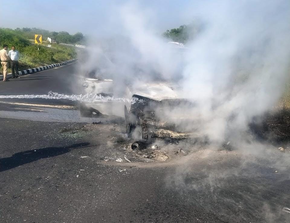 कार में लगी आग को पानी डालकर बुझाते दमकल कर्मी