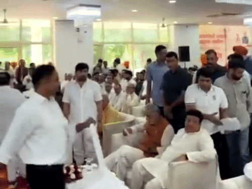 कैबिनेट मंत्री विपुल गोयल और विधायक धनेश अदलखा के बीच कुर्सी रखता एक कर्मचारी।